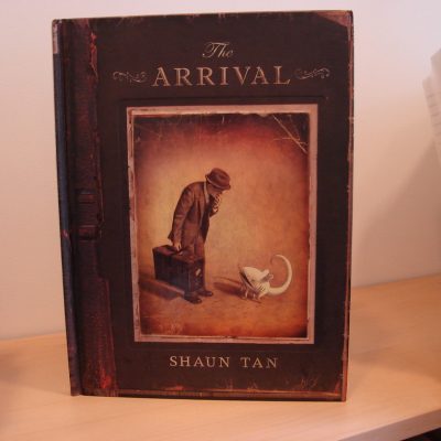 Cover the the book "The Arrival" with the title, author's name and an image featuring a man (an immigrant) with a hat and a suitcase staring down at a mouse-like creature