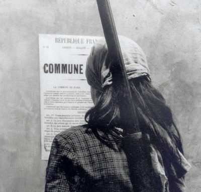 Promotional image for the film La Commune. A woman, her back to the viewer, reads a broadside.