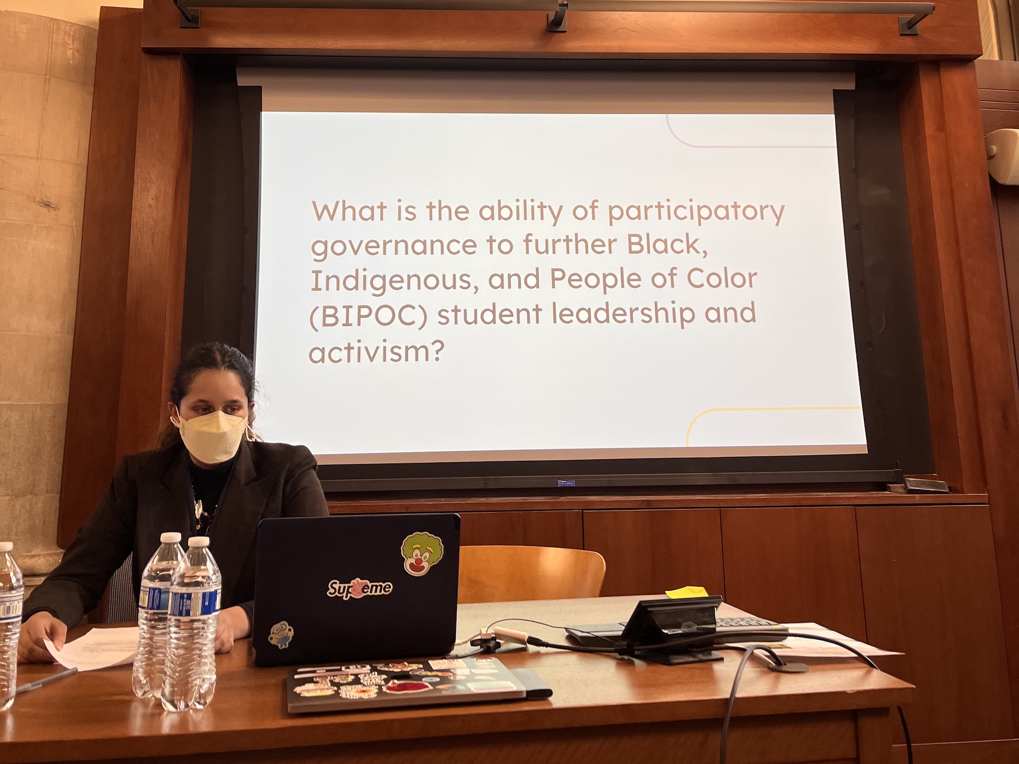 A student presenting at the 2023 Ethnic Studies Symposium in front of a slide that reads "What is the ability of participatory governance to further Black, Indigenous, and People of Color (BIPOC) student leadership and activism?"