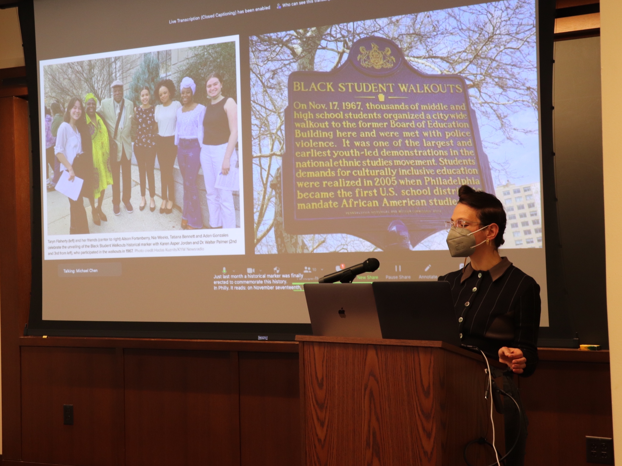 A student stands at a podium in front of a slide with an image of a historical marker that reads "Black student walkouts". From the 2023 Ethnic Studies Symposium.